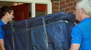 Two delivery technicians carrying a blanket-wrapped item through a doorway